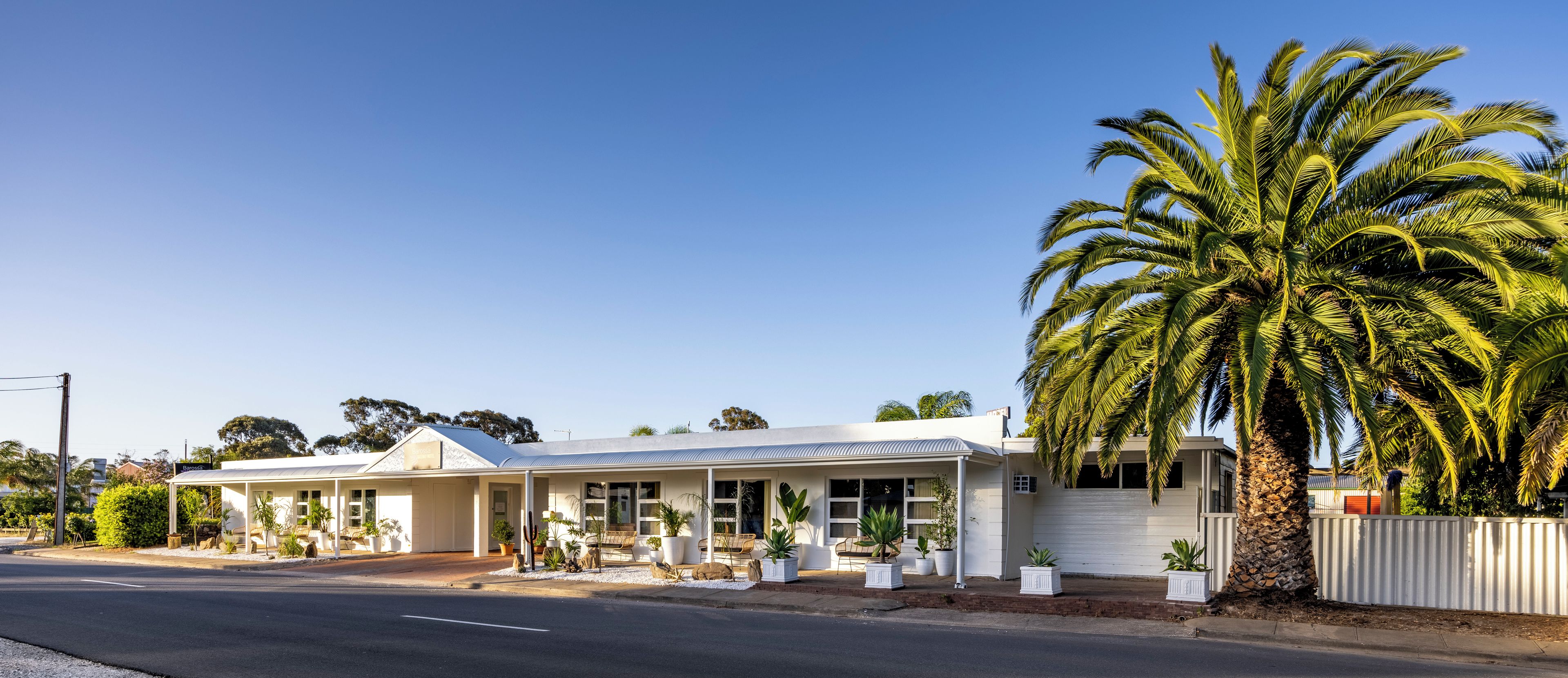Un edificio blanco de dos pisos con un porche cubierto y una palmera grande al frente.