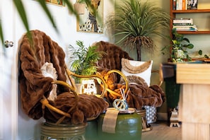 A cozy living room with a large brown fur coat draped over a green chair, a wicker basket, and a potted plant. - Barossa Palms Motel (Nuriootpa)