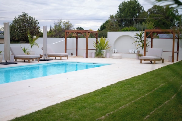 A swimming pool with lounge chairs and a pergola, surrounded by a white wall and greenery. - Barossa Palms Motel (Nuriootpa)