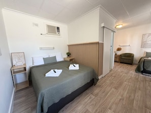 A hotel room with a bed, bedside tables, a plant, a chair, and a door leading to another room. - Barossa Palms Motel (Nuriootpa)