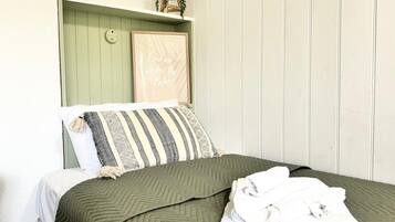 A bed with a green quilt, a striped pillow, and a folded towel on a white mattress.