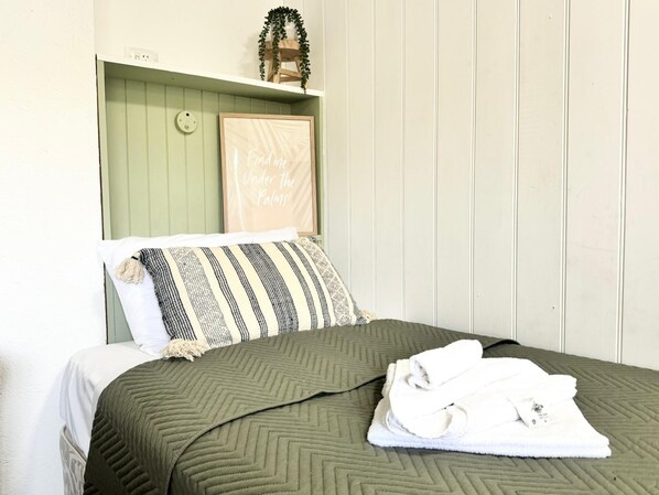 A bed with a green quilt, a striped pillow, and a folded towel on a white mattress. - Barossa Palms Motel (Nuriootpa)