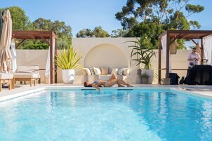 Un área de piscina con sillones de descanso, un espacio de estar techado y plantas en macetas.