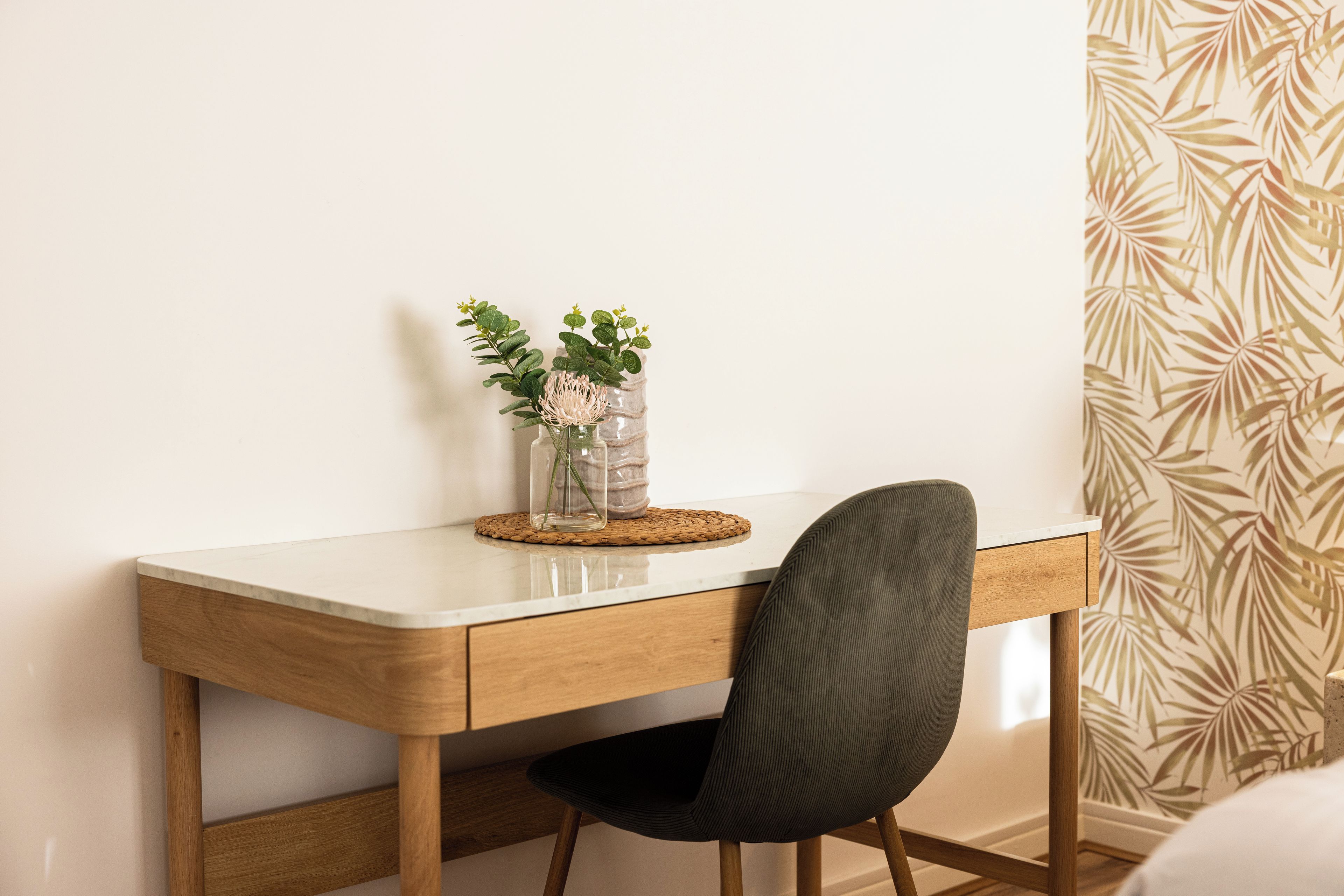 A desk with a vase of flowers, a chair, and a patterned wall.