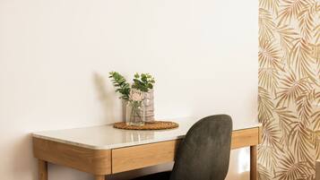 A desk with a vase of flowers, a chair, and a patterned wall.