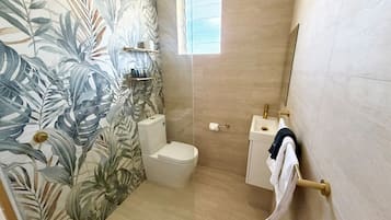 A bathroom with a toilet, a sink, a towel rack, and a shower area.