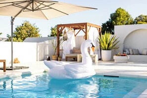 A swimming pool with a swan float, a wooden gazebo, and potted plants.