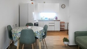 Cozinha compacta com armários brancos, pia e pequena área de refeições com mesa e cadeiras.