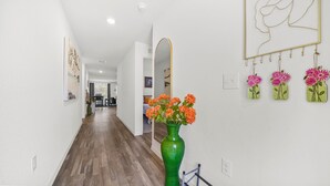 Un pasillo con un jarrón verde de flores, un espejo y arte en la pared.