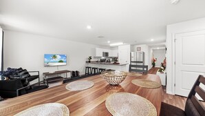 Una cocina moderna con armarios blancos, un microondas y un refrigerador. Hay un comedor con una mesa de madera, sillas negras y individuales tejidos.