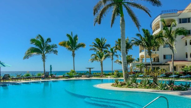 A resort pool with palm trees, lounge chairs, and a building with balconies. - Tortuga TBB 2401 (San José del Cabo)