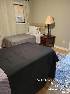 A hotel room with two beds, a nightstand, a lamp, and a window with curtains. - 4-Bedroom Retreat w/Modern Comforts & Local Charm! (Port Arthur)