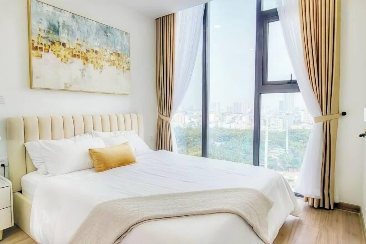 Un dormitorio con una cama grande, una mesita de noche, un cuadro y una ventana con cortinas.