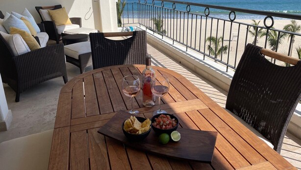 A wooden table with a bottle of wine, two glasses, a bowl of chips, and a lime on a balcony overlooking a beach. - Tortuga Bay TBB 2502 (San José del Cabo)