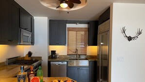 A modern kitchen with dark cabinets, a stainless steel refrigerator, and a ceiling fan. - Tortuga Bay TBB 2502 (San José del Cabo)