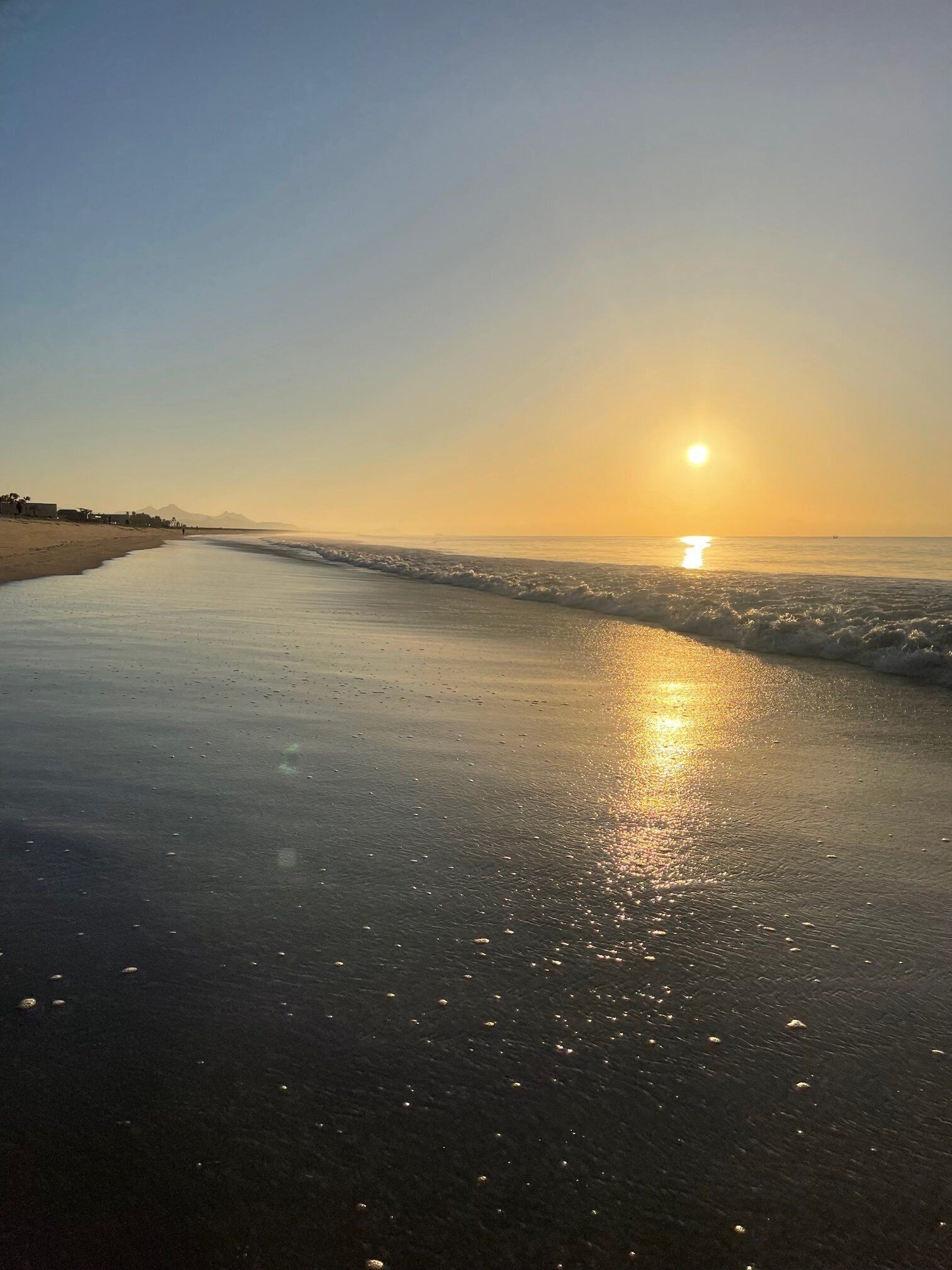 A beach with a sunset, calm waves, and a clear sky.