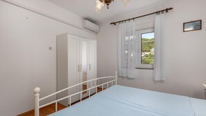 Une chambre à coucher comprenant un lit, une armoire, un appareil de climatisation, une fenêtre avec des rideaux et une vue sur la verdure à l’extérieur.