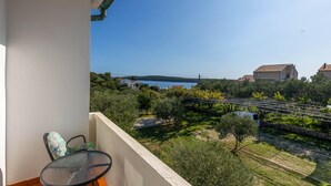 Un balcon avec une table et une chaise, donnant sur un vignoble et un lac, avec des bâtiments visibles au loin.