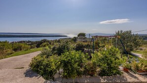 A garden with a swing set, a paved path, and a view of a lake and distant mountains. - Pet friendly apartment in Rab with WiFi (Rab)