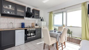 A modern kitchen with a dishwasher, stove, oven, and microwave. There is a dining area with a table and chairs, and a view of the sea through large windows. - Pet friendly apartment in Rab with WiFi (Rab)