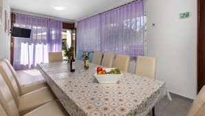 A dining area with a table set for six, surrounded by beige chairs, a bottle of wine, and a bowl of fruit. - Beautiful apartment in Banjol with WiFi (Banjol)