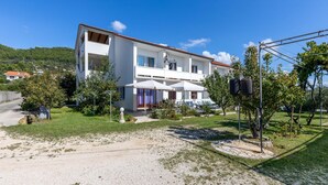 A two-story white building with a red-tiled roof, outdoor seating, and a gravel driveway. - Beautiful apartment in Banjol with WiFi (Banjol)