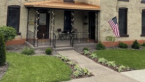 A two-story building with a brick facade, a covered porch with outdoor seating, and an American flag.