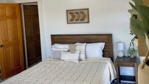 A bedroom with a bed, wooden headboard, a nightstand, a lamp, and a wall-mounted picture.
