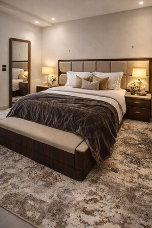Un dormitorio con una cama grande, mesitas de noche, un banco, un espejo y suelo cubierto de alfombra.