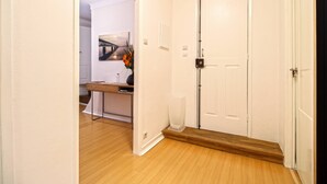 A hallway with a wooden floor, white walls, a white door, and a small table with a vase of flowers. - O Beco - Apart In The Heart Of The City (Viana do Castelo)