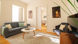 A living room with a grey sofa, a round coffee table, and a dark armchair. There are two paintings on the walls and a plant in the corner. - O Beco - Apart In The Heart Of The City (Viana do Castelo)