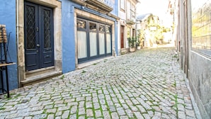 A cobblestone street with buildings on either side, featuring a blue building with a black door and a balcony. - O Beco - Apart In The Heart Of The City (Viana do Castelo)