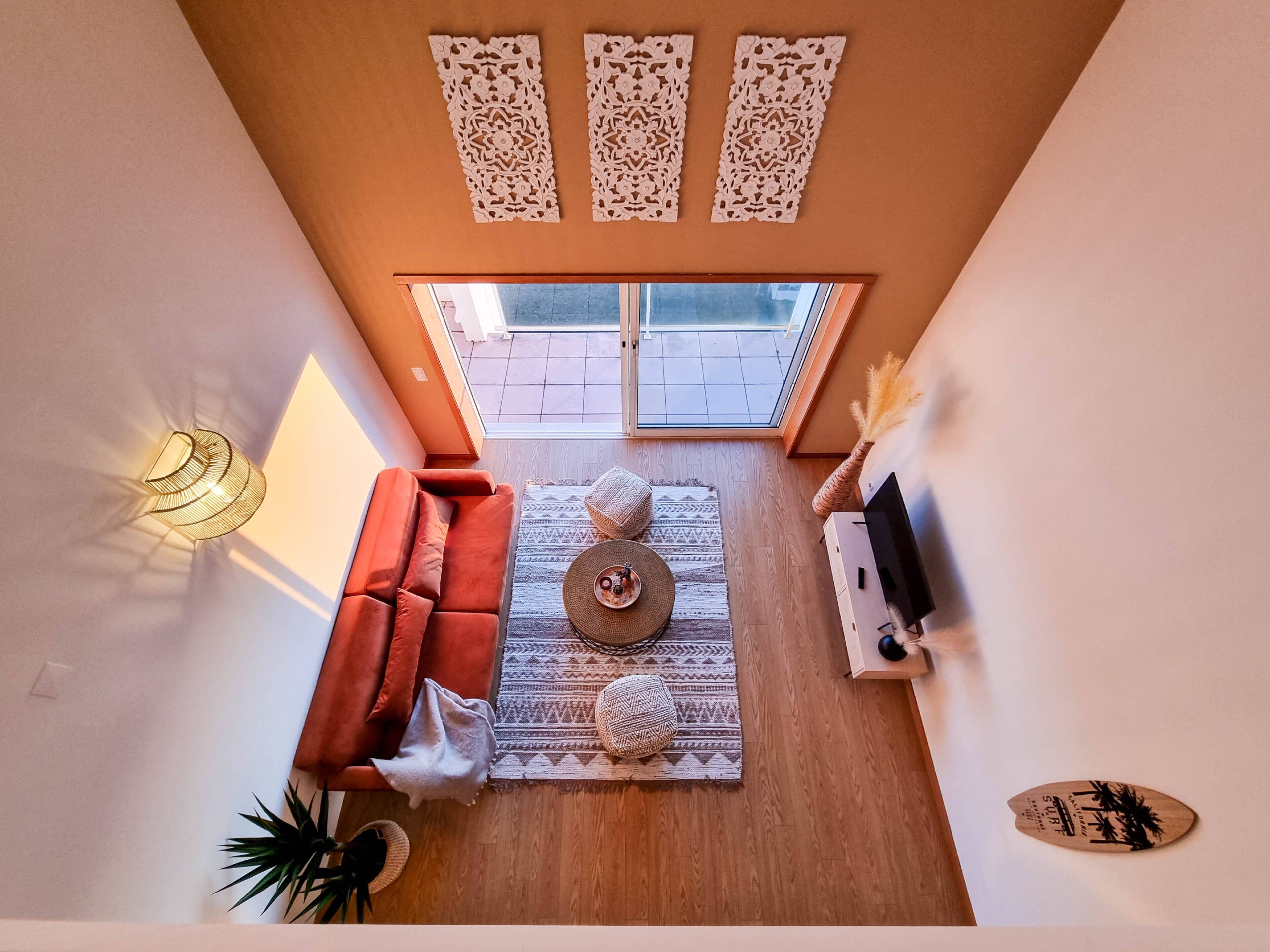 A modern living room with a sofa, a coffee table, and a TV stand. There is a window with a view of the outside.