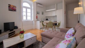 Una sala moderna con un sofá, una mesa de centro con un florero, un televisor y un comedor con sillas y una mesa.