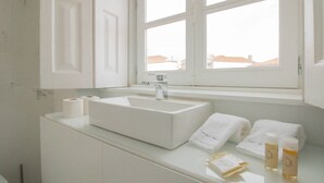 Un baño con un lavamanos blanco, dos toallas y dos botellas sobre el mostrador.