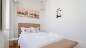 Un dormitorio con una cama, almohadas, un banco, una mesita y obras de arte en las paredes.