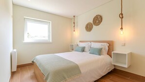 Un dormitorio ordenado con cama, mesitas de noche, ventana y decoración en la pared.