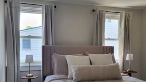 Un dormitorio con una cama grande, dos mesitas de noche y un ventanal con cortinas.