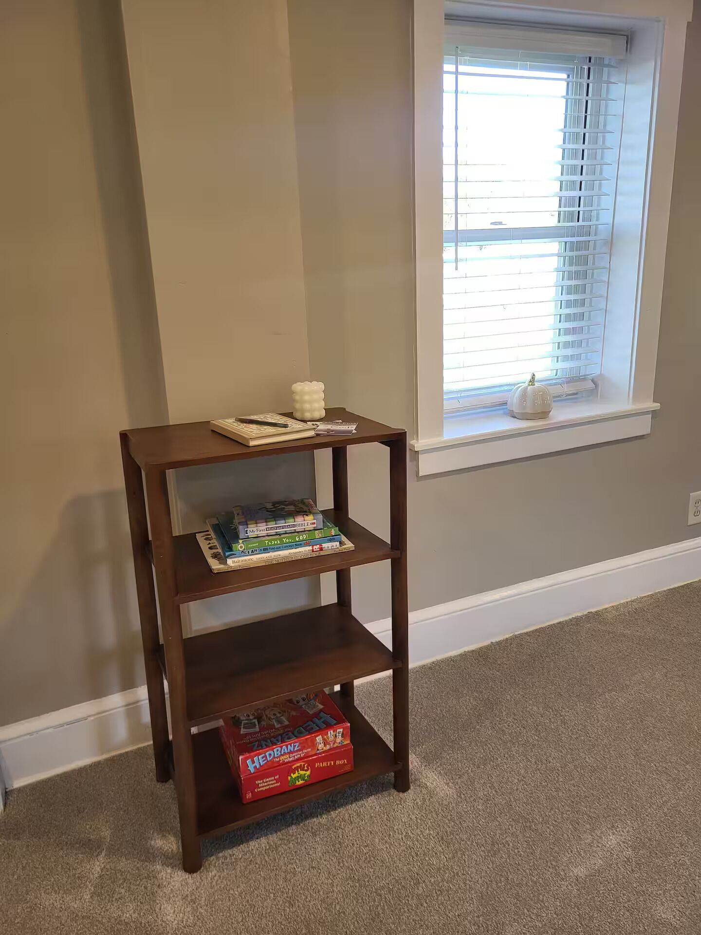 Ein Holzbücherregal mit Büchern und einem Spielkarton an einer Wand mit einem Fenster.