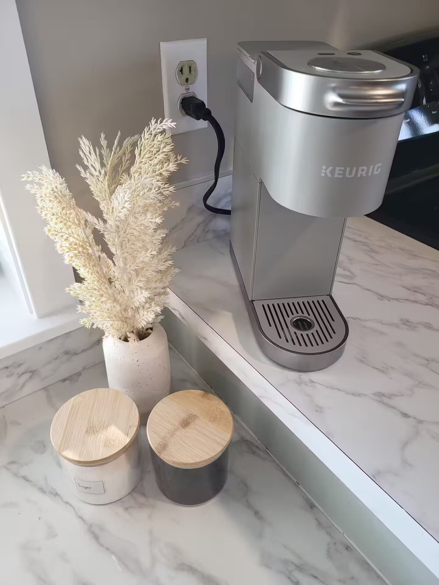 Cuina moderna amb una màquina de cafè Keurig, una planta en test i dos recipients de fusta sobre una superfície de marbre.