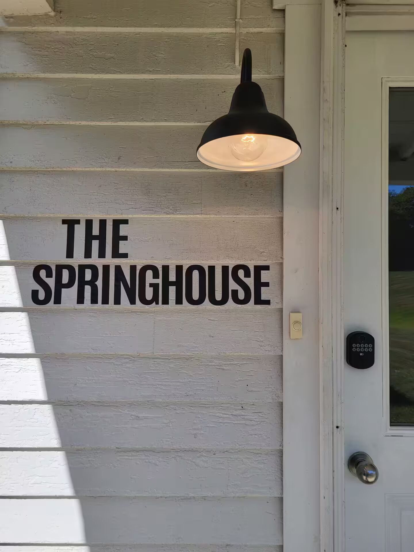 Eine weiße Außenwand mit dem Schriftzug "THE SPRINGHOUSE" und einer schwarzen Pendelleuchte.