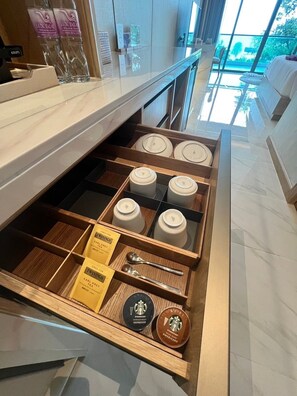 A hotel minibar with neatly organized tea and coffee containers, a spoon, and Starbucks branded items. - Luxtalay Khanom Hotel (Khanom)