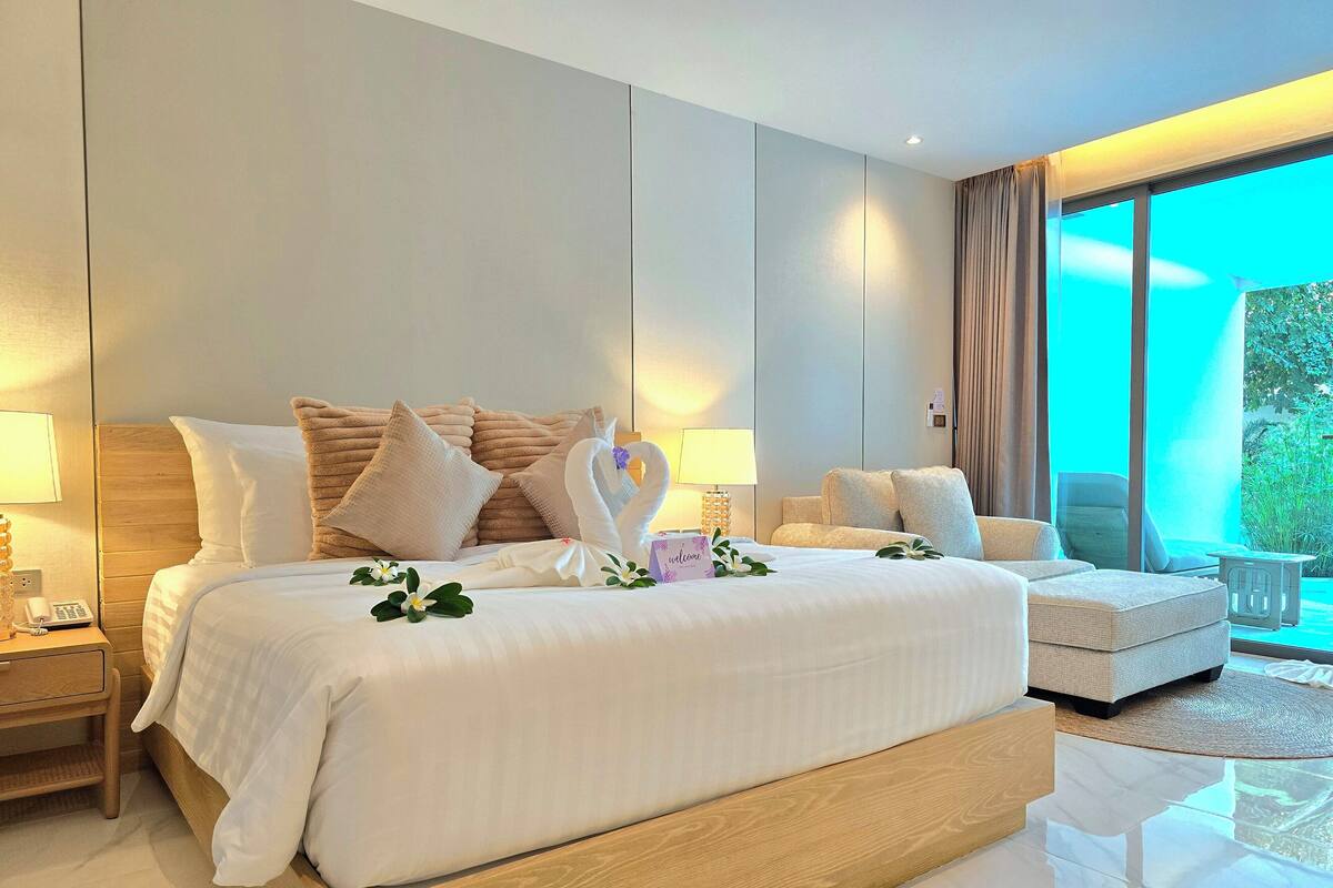 Une chambre d’hôtel moderne avec un grand lit, un canapé, une petite table et une vue sur la verdure par la fenêtre.