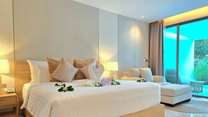A modern hotel room with a large bed, a sofa, a small table, and a view of greenery through the window. - Luxtalay Khanom Hotel (Khanom)