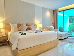A modern hotel room with a large bed, a sofa, a small table, and a view of greenery through the window. - Luxtalay Khanom Hotel (Khanom)