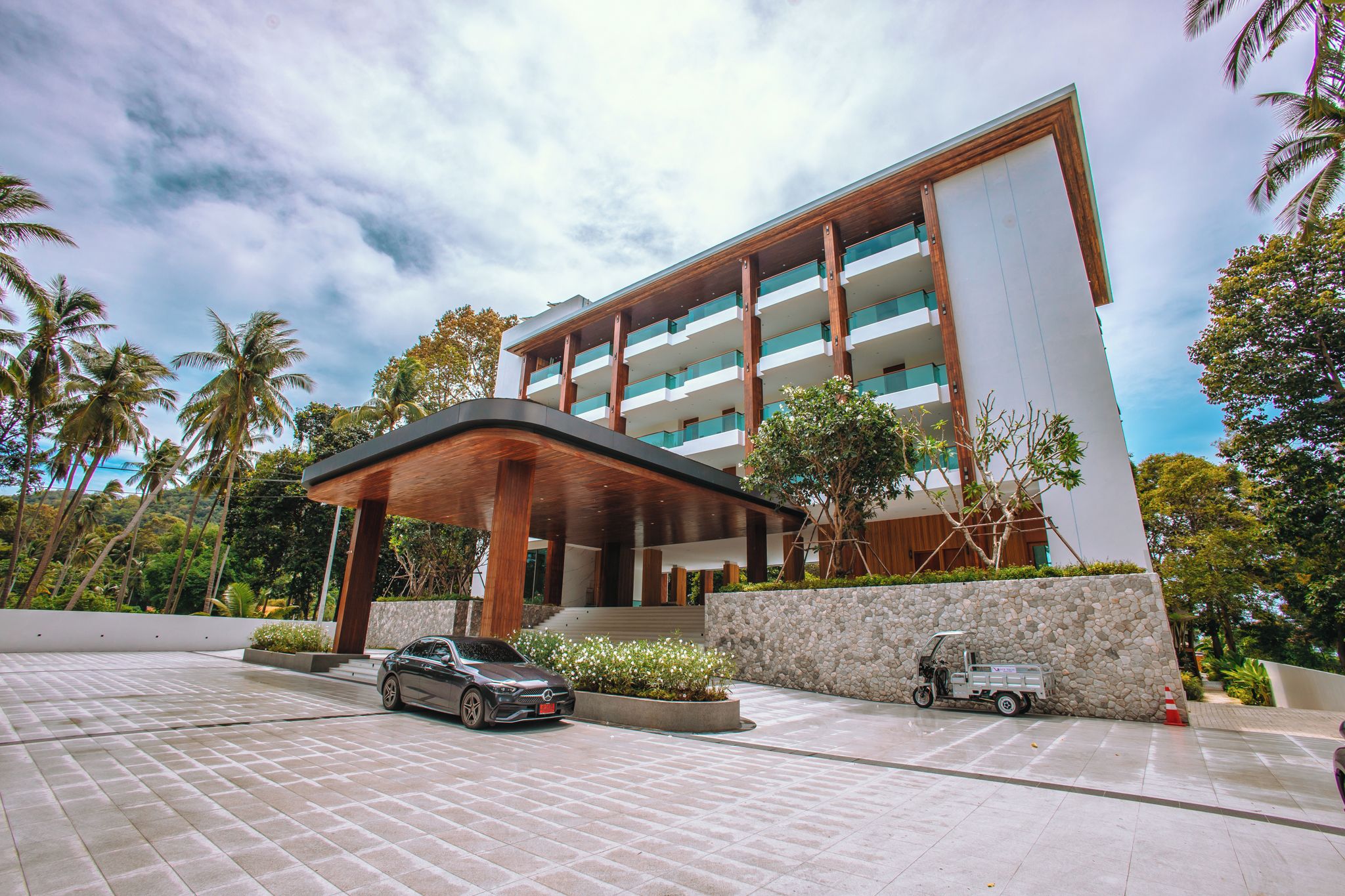 A modern hotel with a covered entrance, a car parked in front, and a golf cart nearby.