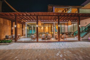 An outdoor dining area with wooden tables and chairs, a covered seating area, and a staircase leading to an upper level.