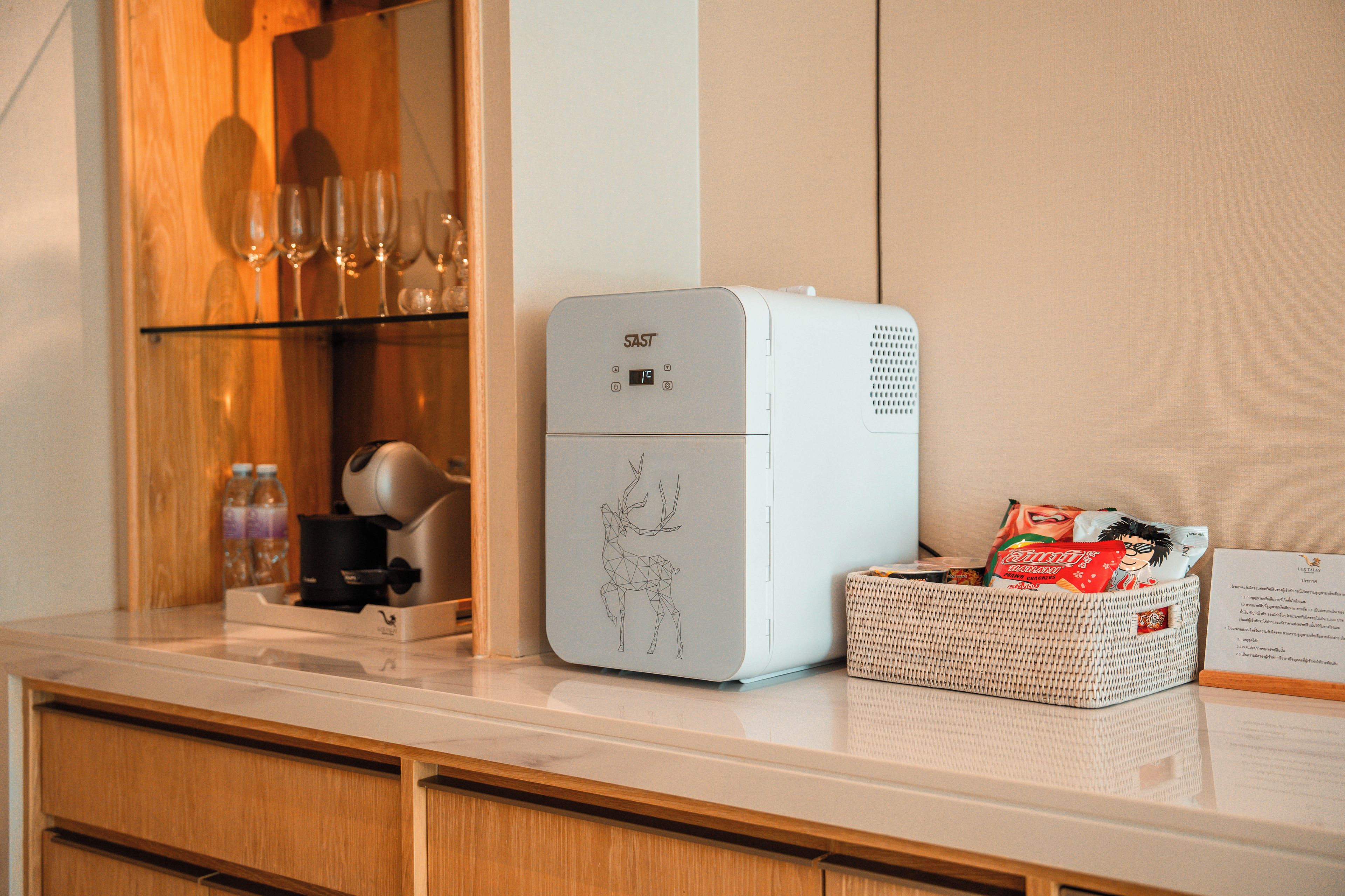 A kitchen with a white refrigerator, wooden cabinets, and a countertop with a basket of snacks and a coffee maker.