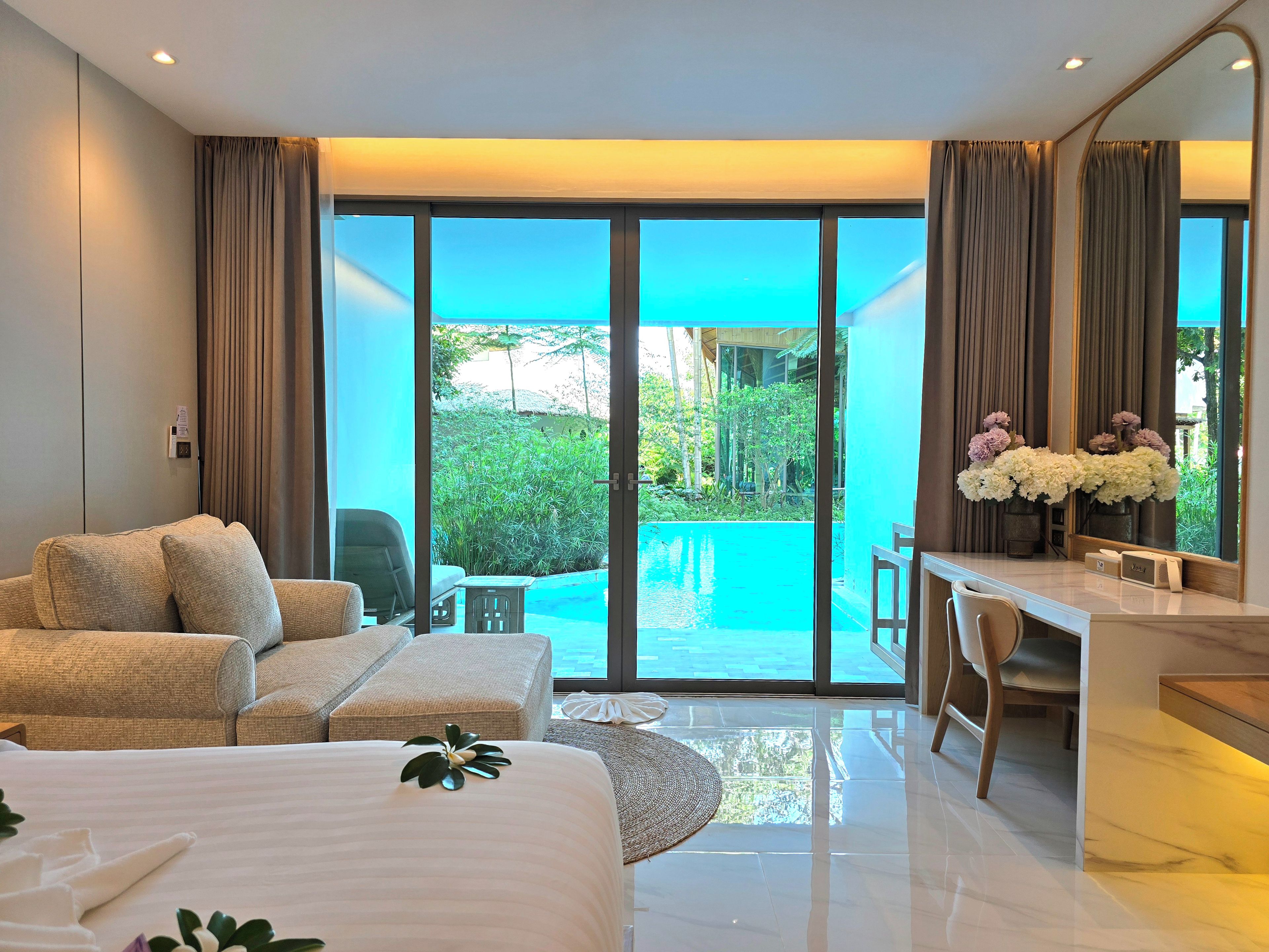 Una habitación de hotel moderna con una cama grande, un escritorio y vistas a una piscina y follaje.
