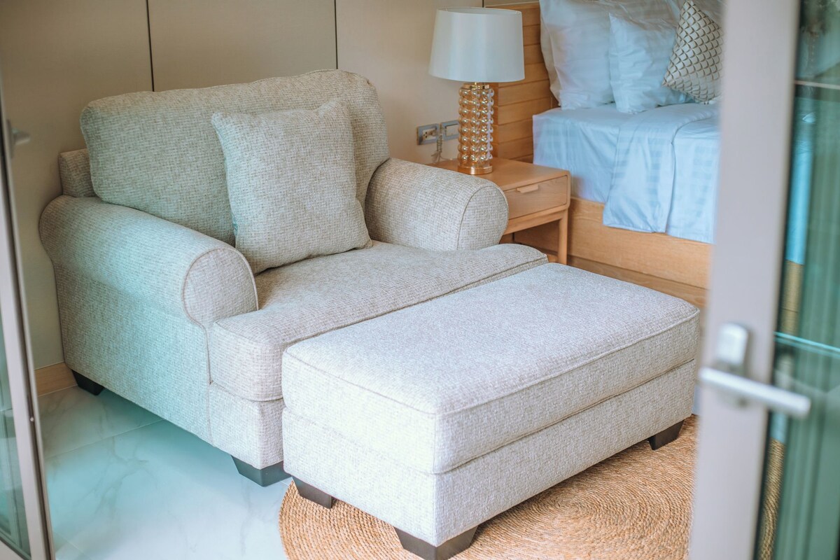 A bedroom with a sofa bed, a bedside table with a lamp, and a bed with pillows and a blanket.